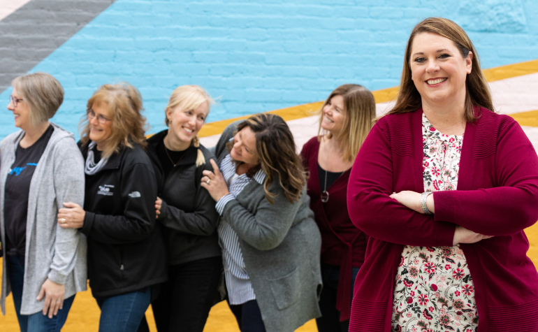 Smiling leader in front of a team of women - Coaches Corner